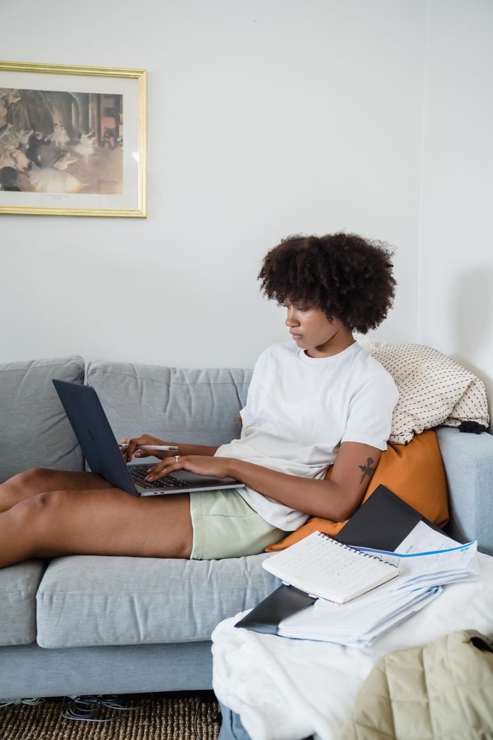 Mastering the First Impression: Your intriguing post title goes here African American woman sitting on couch working remotely on laptop.