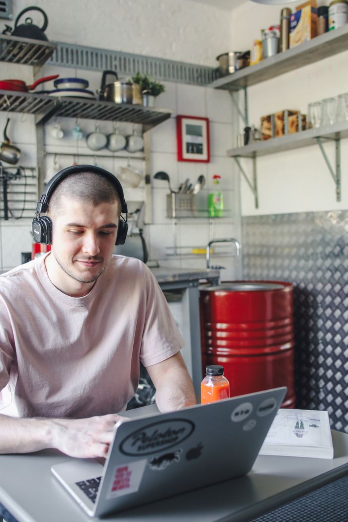 Young man wearing headphones, working on his laptop in a stylish kitchen setting.